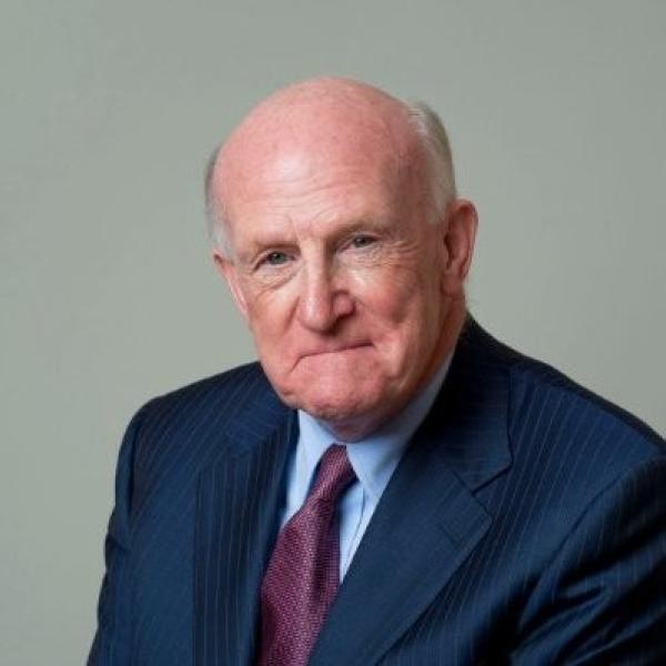 Headshot of Terry Neill wearing a navy suit, light blue shirt and purple tie 