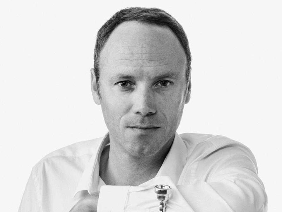 Black and white photo of Clément Saunier dressed in a crisp white shirt leaning on a trumpet