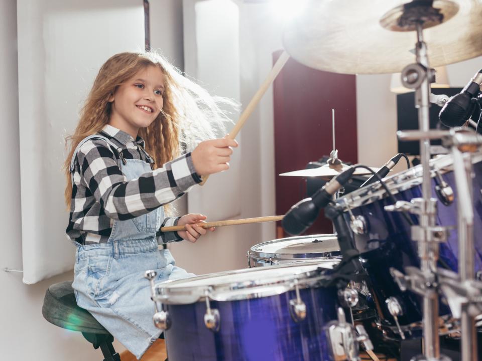 A girl playing smiling while playing the drum kit