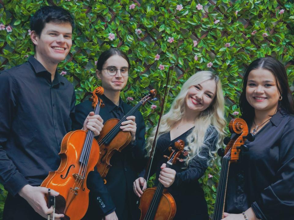 Four string musicians standing holding their instruments against a flower backdrop