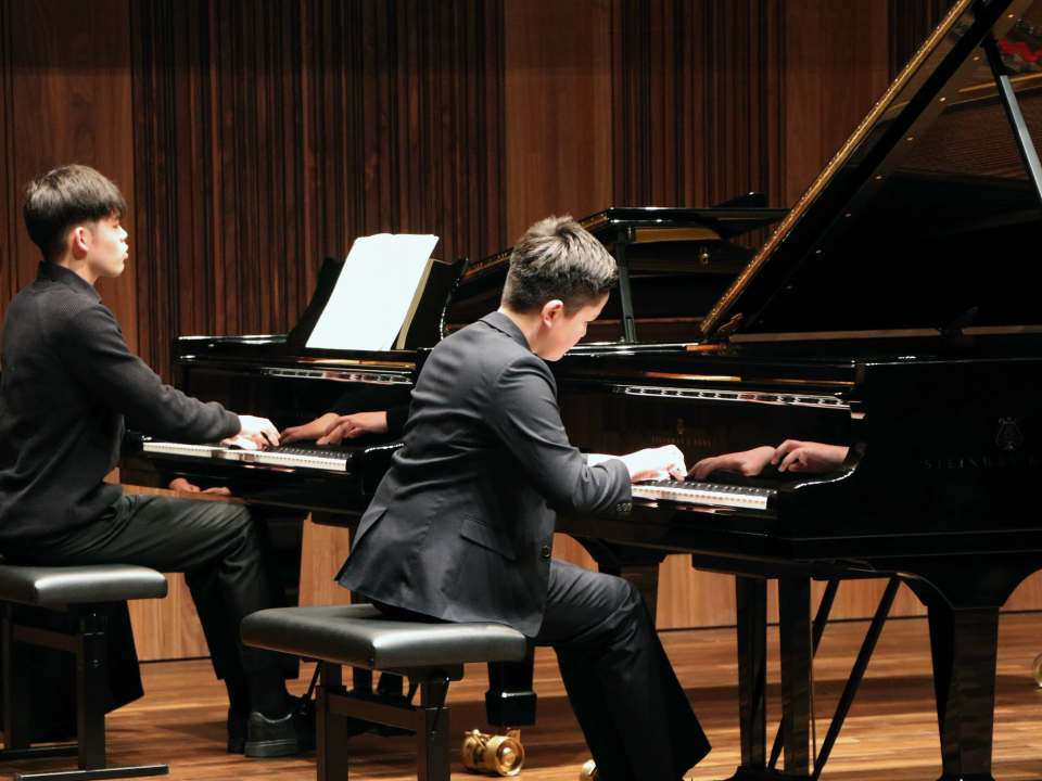 Two pianists perform side by side on stage at the Whyte Recital Hall