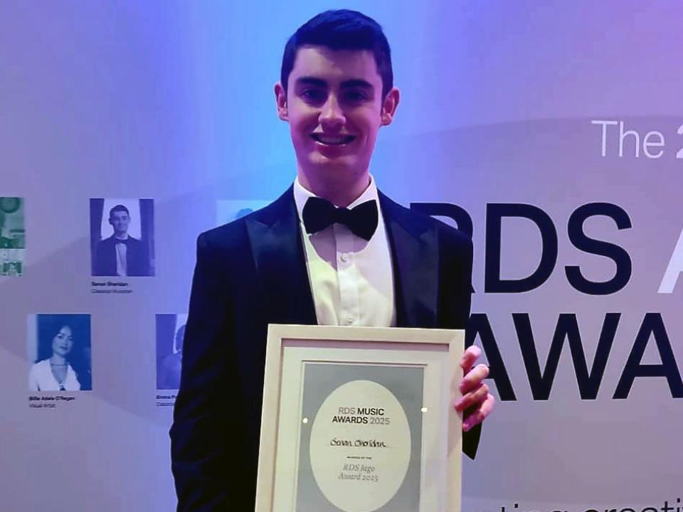 Junior RIAM pianist Senan Sheridan stands in front of an RDS Music Awards backdrop, smiling and holding his framed 2025 RDS Jago Award certificate.