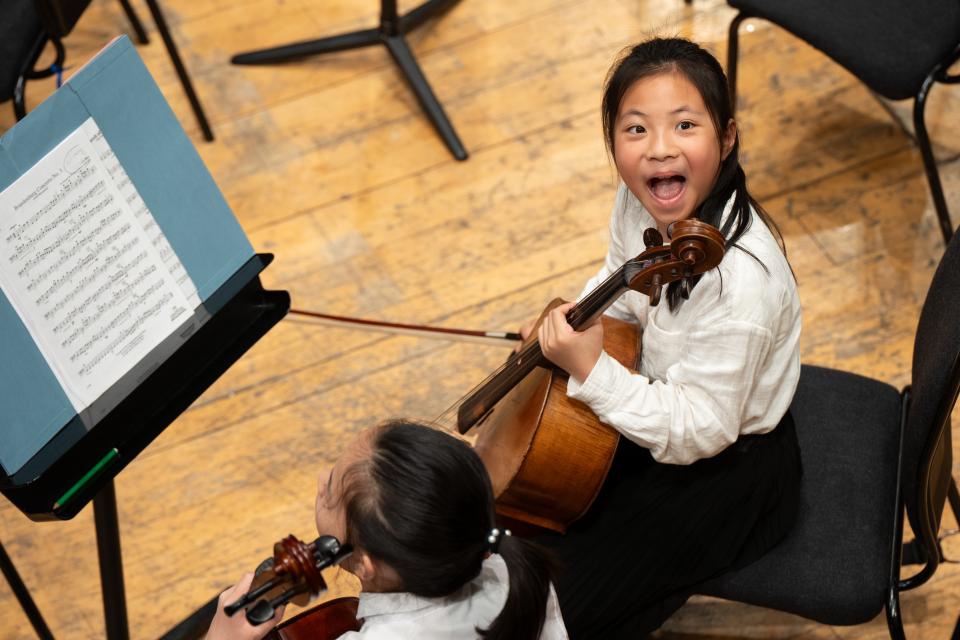 An image of a child smiling playing the cello