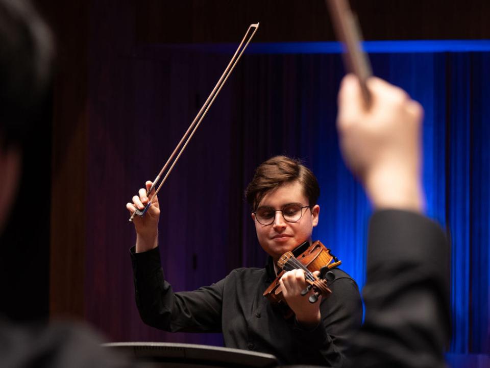 A young male student holds aloft his violin bow after finishing a performance