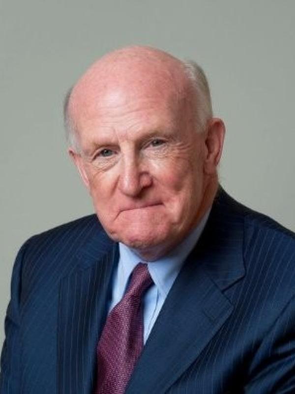 Headshot of Terry Neill wearing a navy suit, light blue shirt and purple tie 